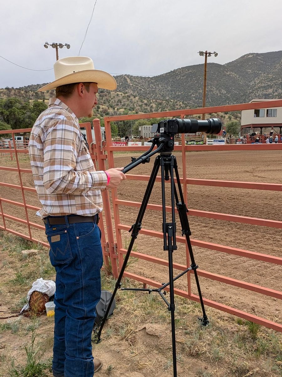 James Roth in a cowboy hat operating a camera on a tripod at an outdoor event.